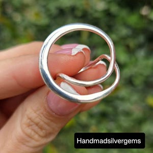 May include: A close-up of a silver ring with a unique, intertwined design. The ring features two connected circular bands, one larger than the other. The text "Handmadsilvergems" is displayed in a black rectangle at the bottom of the image.