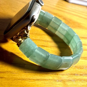 May include: A silver Apple Watch with a green jade beaded band. The band is made of smooth, rounded beads that are connected together.