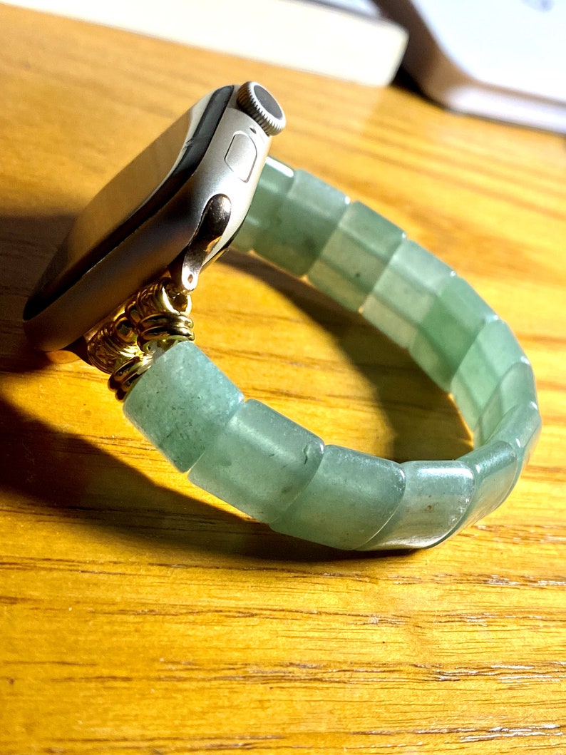 May include: A silver Apple Watch with a green jade beaded band. The band is made of smooth, rounded beads that are connected together.