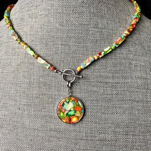May include: A colorful, multi-colored, multi-faceted stone necklace with a matching pendant. The necklace has a silver toggle clasp.