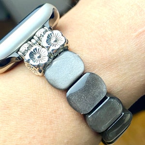 May include: A silver watch band with a floral design and gray stone beads.
