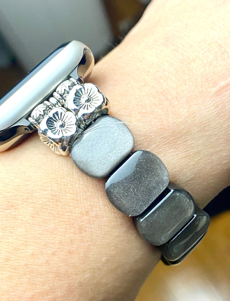 May include: A silver watch band with a floral design and gray stone beads.
