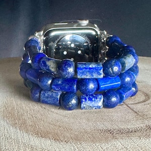 Könnte beinhalten: Eine silberne Apple Watch mit einem blauen Lapislazuli-Perlenarmband. Das Armband besteht aus mehreren Reihen von Perlen, einige rund und einige rechteckig.