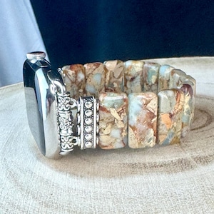 May include: A silver and brown patterned watch band with a silver clasp. The band is made of rectangular stones and has a decorative silver accent.