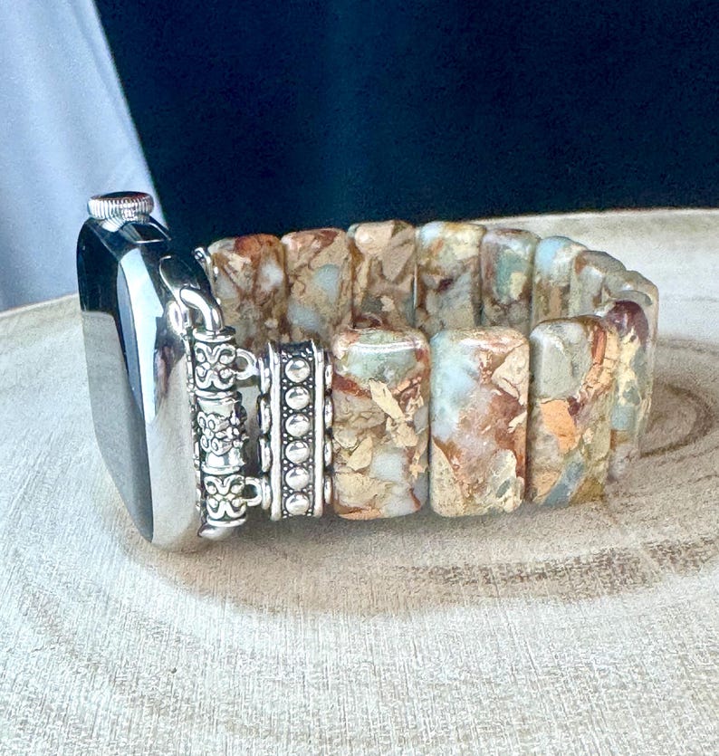 May include: A silver and brown patterned watch band with a silver clasp. The band is made of rectangular stones and has a decorative silver accent.