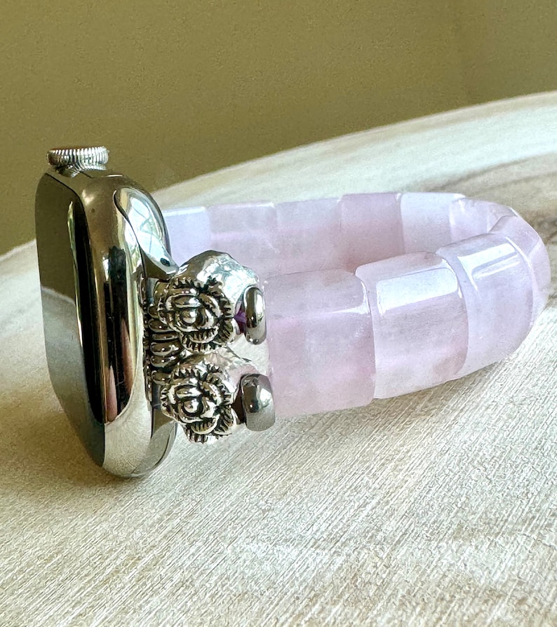 May include: A silver Apple Watch with a pink rose quartz band. The band is made of smooth, polished stones and has a silver clasp.