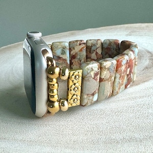 May include: A beige and brown patterned Apple Watch band with a gold clasp and decorative beads. The band is made of stone and has a floral design.