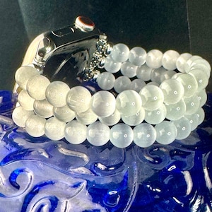 May include: A white beaded watch band made of round, smooth, opaque beads. The band is wrapped around a silver Apple Watch.