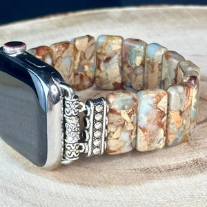 May include: A silver and brown Apple Watch band made of rectangular, patterned stones. The band has a silver clasp with decorative details.