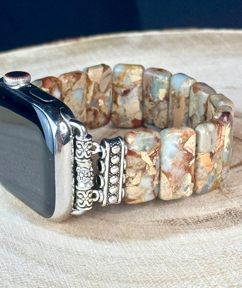 May include: A silver and brown Apple Watch band made of rectangular, patterned stones. The band has a silver clasp with decorative details.