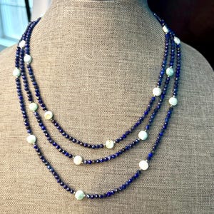 May include: A three-strand necklace featuring dark blue faceted beads and interspersed with round, light blue and white beads. The necklace is displayed on a neutral-toned mannequin.