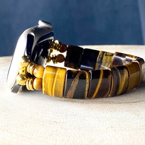 May include: A gold and brown tiger's eye beaded watch band for an Apple Watch.