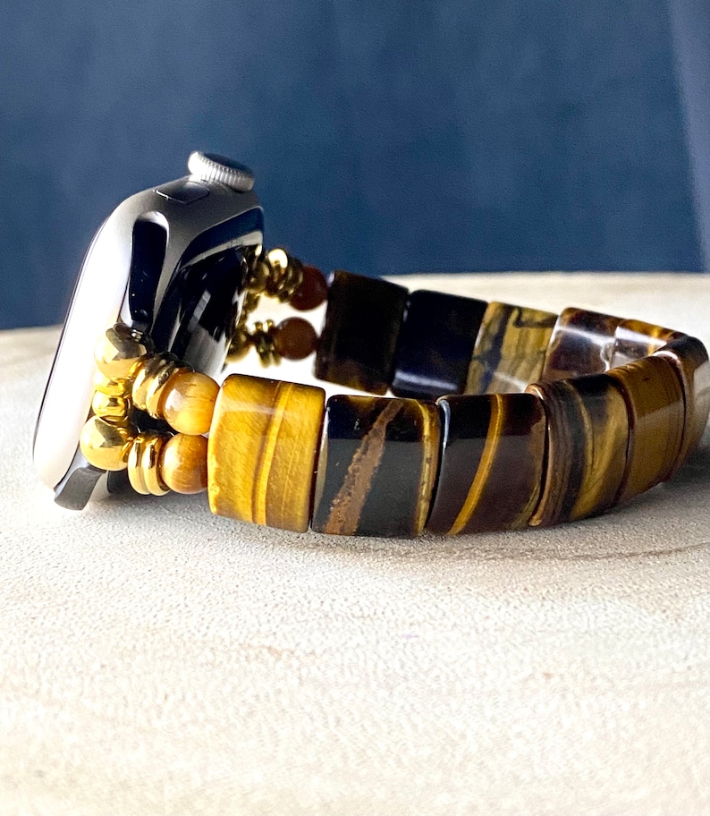 May include: A gold and brown tiger's eye beaded watch band for an Apple Watch.