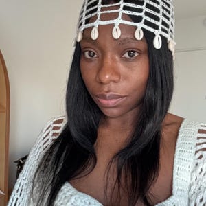 Op de afbeelding: Een witte gehaakte hoed met een schelpbezetting. De hoed heeft een brede rand en een losse pasvorm. De hoed is gemaakt van zacht, lichtgewicht garen.