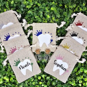 May include: Set of ten small hessian bags with a tooth design and a crown. The bags are decorated with glitter and have the names "Noah" and "Sophia" written on them.