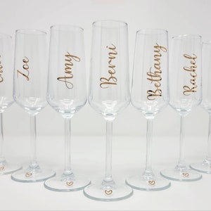 May include: Seven clear champagne flutes with gold lettering. Each glass has a different name: Chloe, Zoe, Amy, Berni, Bethany, Rachel, and Mum. A small gold heart is at the base of each glass.
