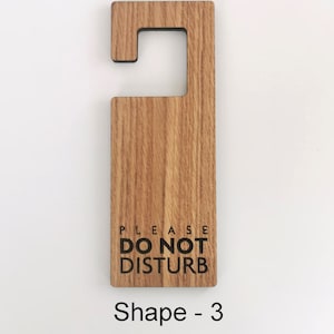 May include: Wooden door hanger with the text "PLEASE DO NOT DISTURB" in black lettering. The hanger is shaped like a rectangle with a cut-out handle at the top. The wood has a natural grain pattern. Shape - 3