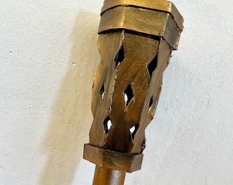 Könnte beinhalten: Eine dekorative Fackel mit metallisch goldener Oberfläche. Der obere Teil hat rautenförmige Aussparungen, und der Griff hat eine passende braune Farbe. Die Fackel ist für dekorative Zwecke bestimmt.