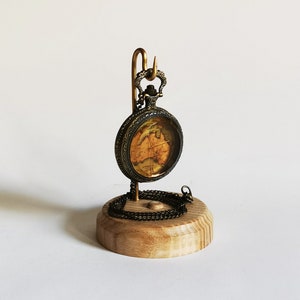 May include: A gold pocket watch with a map design on the face is displayed on a wooden stand. The watch is attached to a chain.