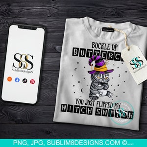 Könnte beinhalten: Weißes T-Shirt mit einer Grafik einer grimmigen Katze mit Hexenhut. Der Text lautet "Buckle Up Buttercup, You Just Flipped My Witch Switch." Das Design beinhaltet Sterne und Monde. Ein Telefon und ein Etikett mit Logo sind ebenfalls sichtbar.