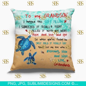 Puede incluir: Un cojín decorativo con una escena de playa con dos tortugas marinas azules en una orilla arenosa. El cojín tiene el texto "To my Grandson...Love, Grandma". El fondo tiene un océano turquesa y una playa de color beige claro.