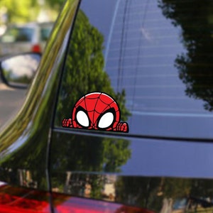 May include: A red and blue car with a Spider-Man sticker on the rear window. The sticker shows Spider-Man peeking out from behind a wall. The car has the text "DOOZY DECALS" on the rear window. The text "WATERPROOF & UV PROTECTED" and "4+ YEARS LIFESPAN" are printed at the bottom of the image. The text "PREMIUM QUALITY VINYL DECALS" is printed at the bottom right of the image.
