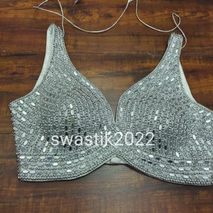 May include: A silver bra with a V-neckline, covered in small, round, mirrored sequins. The bra has adjustable straps and a hook and eye closure in the back.
