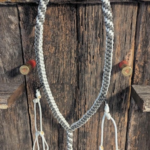 May include: A braided rope hunting dog collar in gray and white, with a matching leash. The collar is suspended on a wooden background, with two shotgun shells on either side.