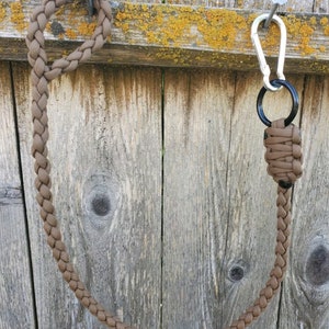 May include: A brown paracord keychain with a silver carabiner and a brown paracord loop. The keychain is hanging from a nail on a wooden fence.
