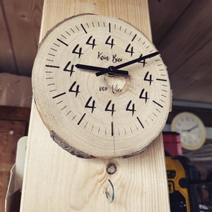 Könnte beinhalten: Eine Holzuhr mit schwarzen Zeigern und einem schwarzen Zifferblatt. Die Uhr ist aus einer Baumscheiben gefertigt und hat den Text "Kein Bier vor Vier" auf dem Zifferblatt.