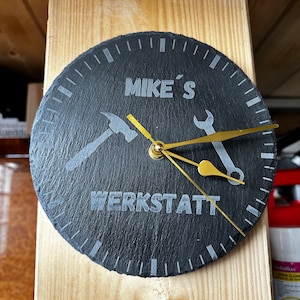 Könnte beinhalten: Schwarze Schieferuhr mit goldenen Zeigern und einem Hammer- und Schraubenschlüssel-Design. Das Zifferblatt der Uhr zeigt "MIKE'S WERKSTATT".