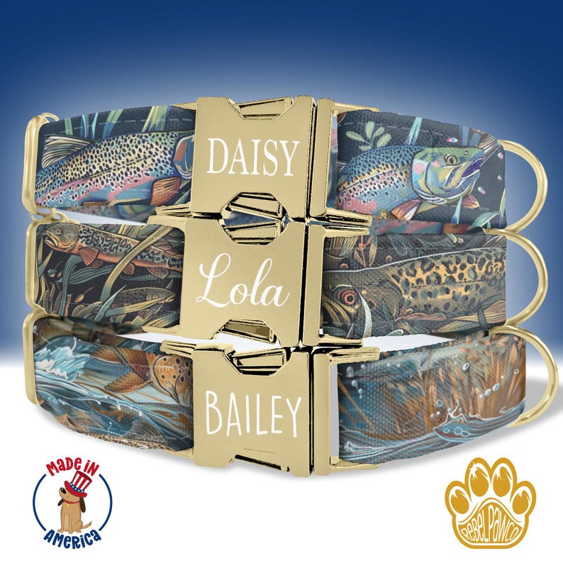 May include: Three dog collars with a fishing theme. The collars are made of a dark blue fabric with a pattern of fish and water. The collars have gold buckles with the names "Daisy", "Lola", and "Bailey" engraved on them.