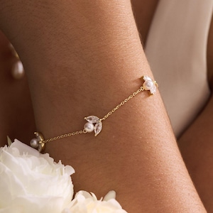 May include: A delicate gold bracelet with pearl and crystal accents. The bracelet features a fine chain with leaf-shaped clusters of crystals and pearls. The design is elegant and suitable for special occasions.