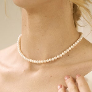 May include: A simple pearl necklace with a delicate, classic design. The necklace is made of small, white pearls and is perfect for adding a touch of elegance to any outfit.