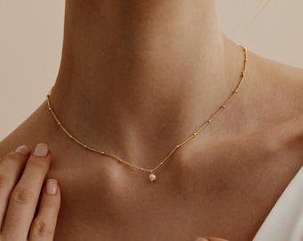 May include: A delicate gold chain necklace with a single pearl pendant. The chain is made of small, evenly spaced gold beads.