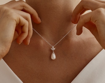 May include: A delicate silver chain necklace with a pearlescent drop pendant and a small cluster of clear cubic zirconia stones.