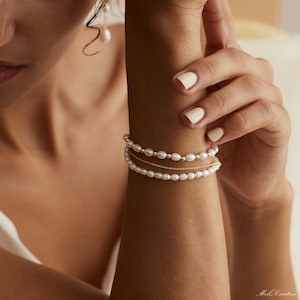 May include: A set of three bracelets featuring a delicate gold chain and two strands of white pearls.