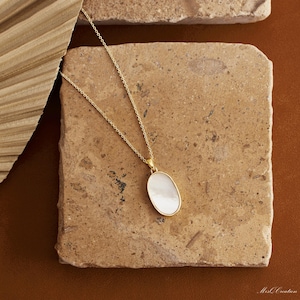 May include: A gold chain necklace with a white oval pendant. The pendant is made of mother of pearl and has a smooth, polished finish.