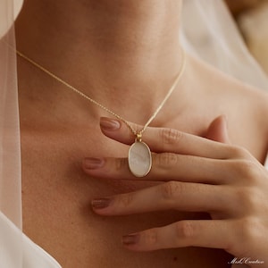 May include: A gold chain necklace with a white oval pendant. The pendant has a smooth, pearlescent finish.