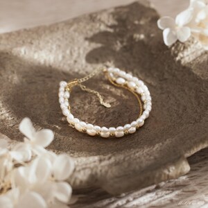 May include: A delicate gold chain bracelet with two rows of white pearls. The bracelet is adjustable and has a simple, elegant design.