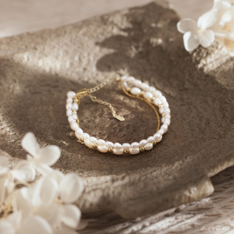 May include: A delicate gold chain bracelet with two rows of white pearls. The bracelet is adjustable and has a simple, elegant design.