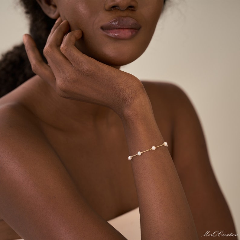 May include: A delicate gold chain bracelet with small white pearls. The bracelet is on a person's wrist.