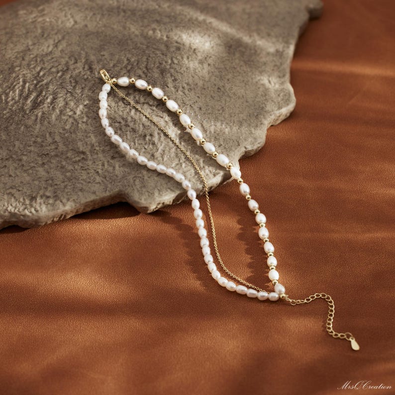 May include: A delicate gold chain necklace with a layered pearl strand. The necklace features a small gold charm at the end.