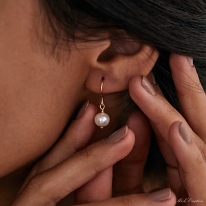 May include: Gold hoop earrings with a single white pearl dangling from each hoop.