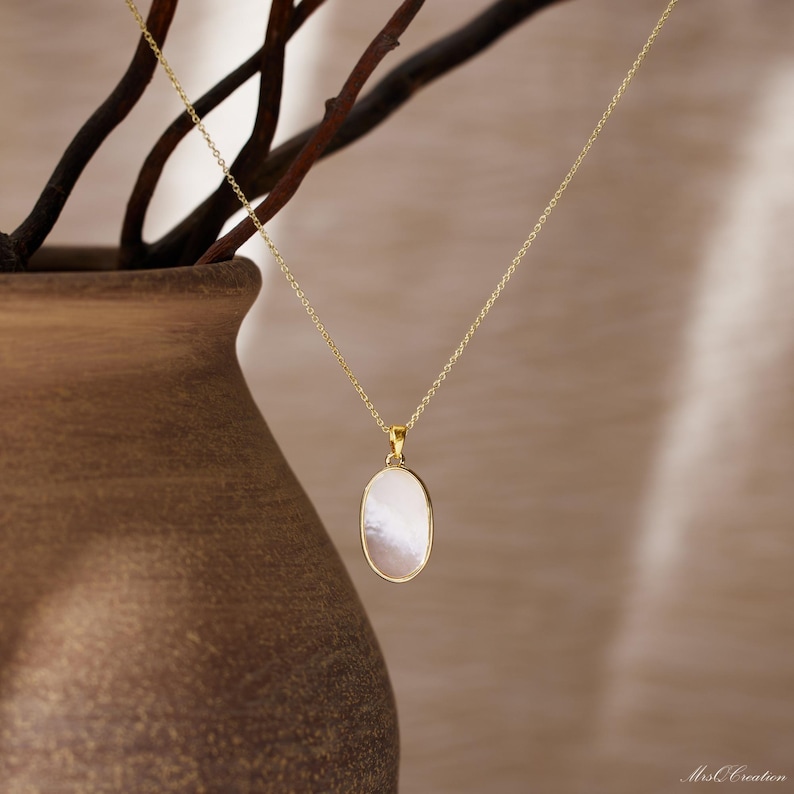 May include: A gold chain necklace with a white oval pendant. The pendant is made of mother of pearl.