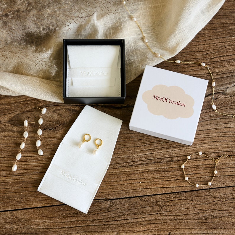 May include: A set of pearl earrings and a pearl bracelet in a white box with the text "MrsQCreation". The jewelry is on a wooden surface with a white fabric in the background.