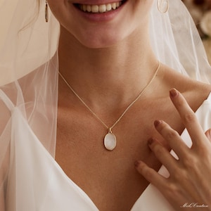 May include: A gold chain necklace with a white oval pendant. The pendant has a textured surface.