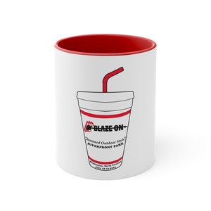 Puede incluir: Taza de cerámica blanca con interior rojo, con un gráfico de un vaso de refresco con una pajita roja. El diseño del vaso incluye el texto "BLAZE ON" y "Jammed Outdoor Style Riverfront Park Wilmington, North Carolina July 18-19-2023".