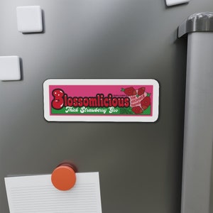 Puede incluir: Una pegatina rosa y verde con el texto "Blossomlicious" y "Thick Strawberry Goo". La pegatina también presenta un gráfico de fresa roja y el texto "the ultimate band".