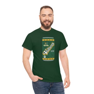 May include: A green t-shirt with a graphic of a green and yellow can of "Vulture's" ginger ale. The can has a wooden texture and a yellow label with the text "Vulture's The Original Ginger Ale".